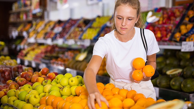 Chica comprando naranjas en una frutería