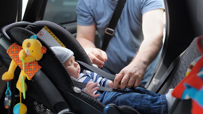 hombre colocando a un bebé de pocos meses en una sillita de coche - sillitas para recién nacidos