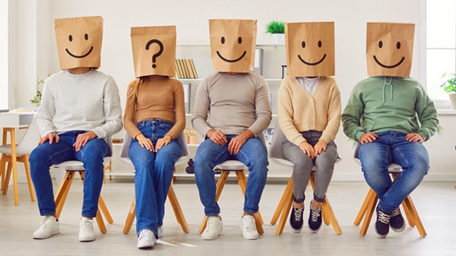 Grupo de gente con unas bolsas de papel en la cabeza en la que está dibujada una cara sonriente; una de ellas tiene dibujada una interrogación